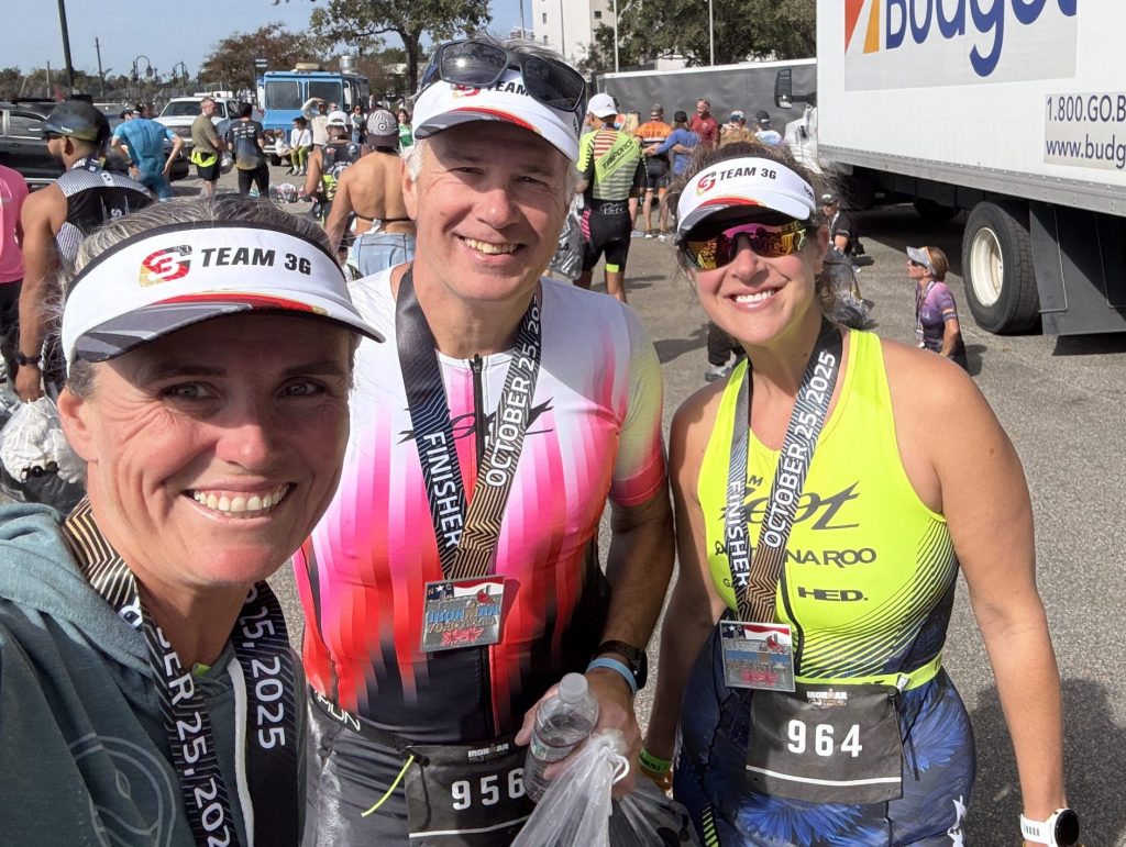 Triathlon coach Erin Byrge with athletes after a race wearing medals and Team 3G visors showing successful coaching results