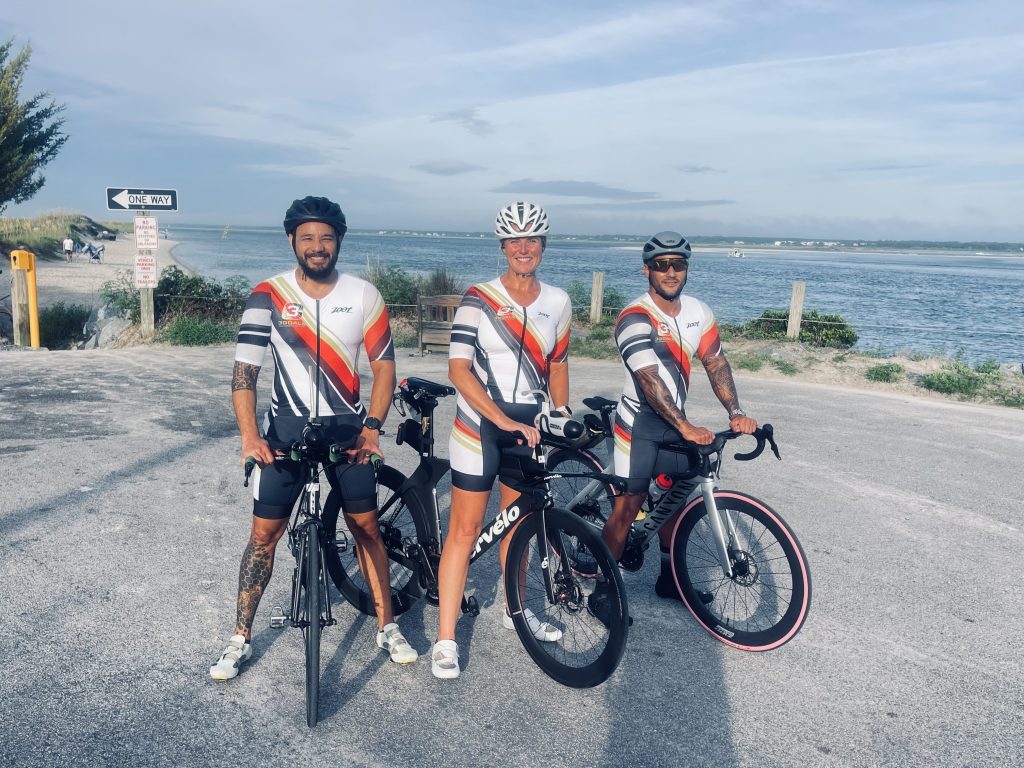 Three Team 3G athletes in matching kits with their bicycles beside the water.